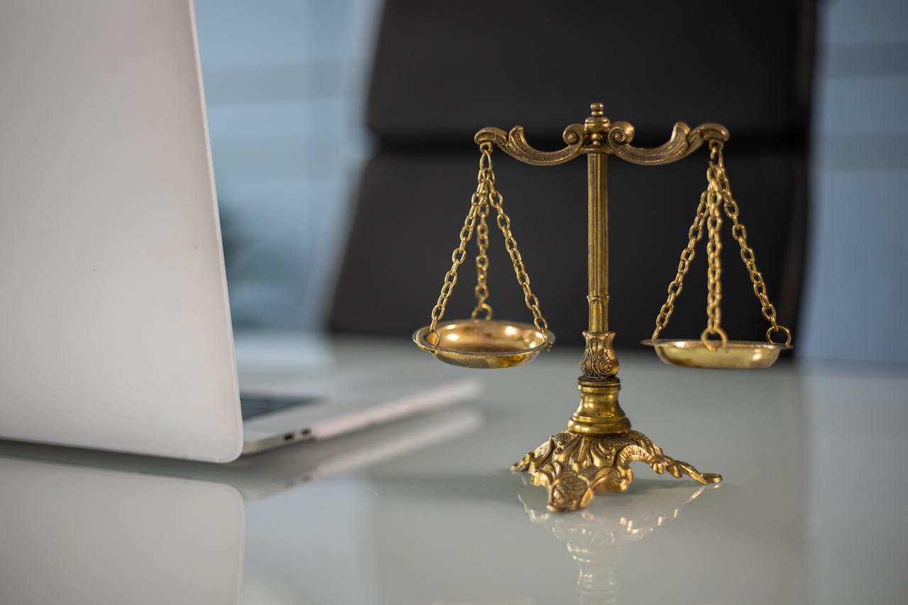 TUTVUSTUS Golden justice scales on a desk beside a laptop, symbolizing law and balance.