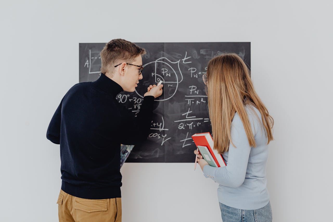 TUTVUSTUS Two students working together on trigonometric equations on a blackboard, enhancing learning.