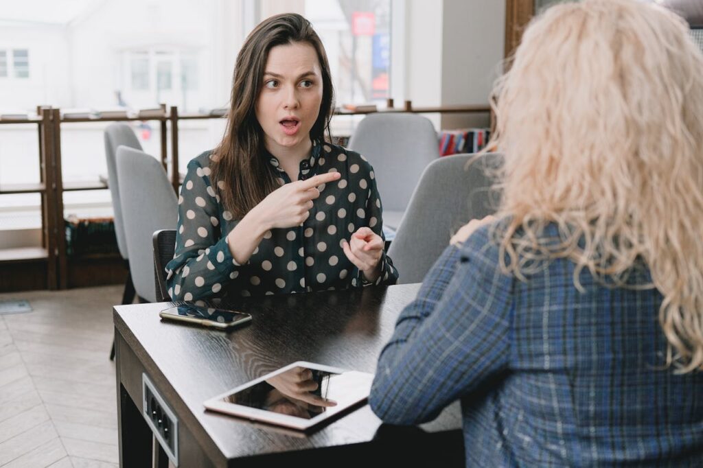 Two women in a lively discussion at a café, with expressive hand gestures and mobile devices on the table.