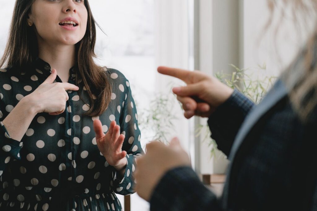 A young woman in a polka dot dress gestures expressively during a conversation indoors.